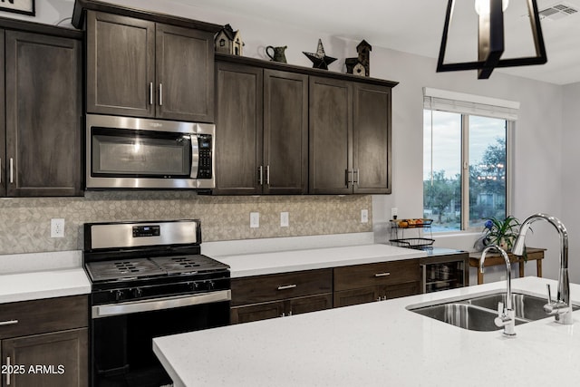 kitchen with gas range oven, stainless steel microwave, visible vents, decorative backsplash, and a sink