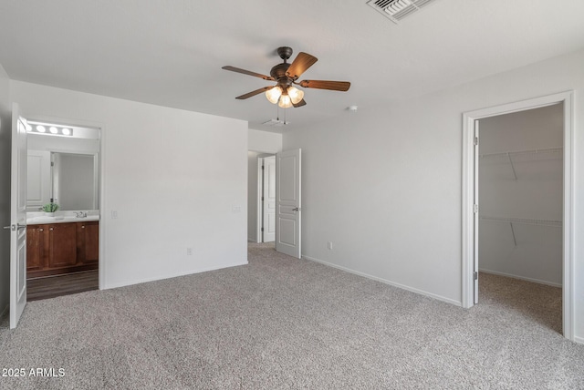 unfurnished bedroom with ceiling fan, ensuite bathroom, a walk in closet, light colored carpet, and a closet