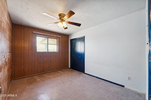 unfurnished room with a textured ceiling, wooden walls, baseboards, and a ceiling fan