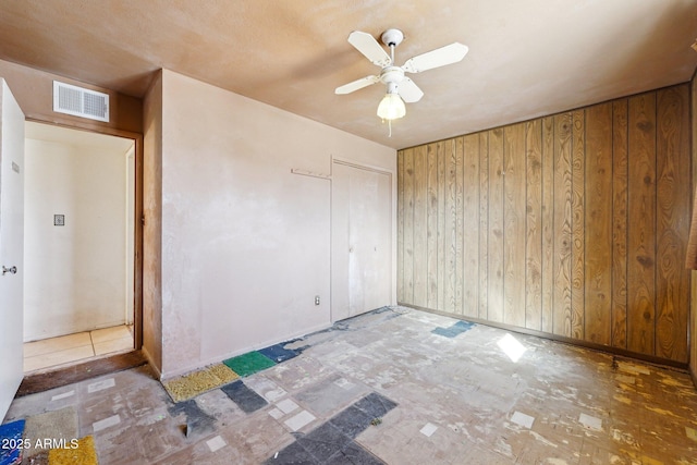 spare room featuring ceiling fan, visible vents, and wooden walls