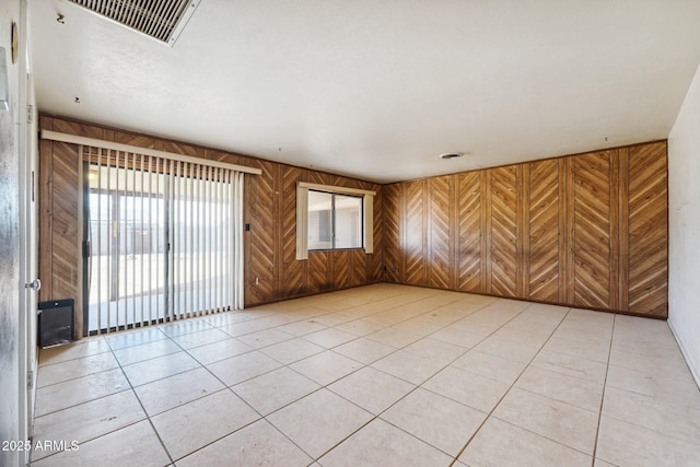 empty room featuring light tile patterned flooring, visible vents, and wooden walls