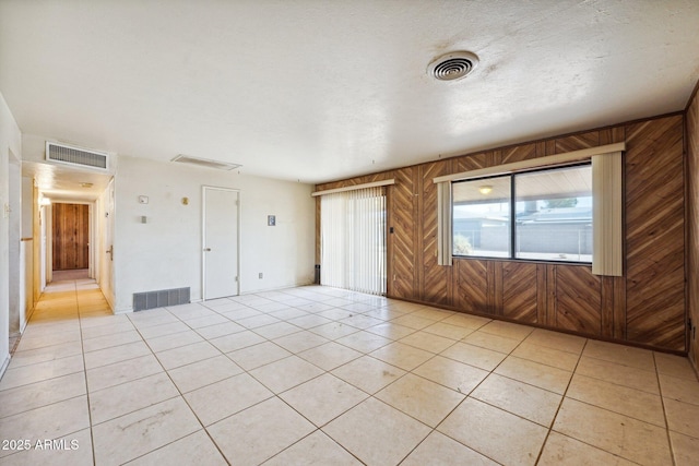 spare room featuring light tile patterned floors, wooden walls, and visible vents