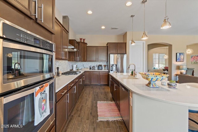 10914 E Tarragon Ave, Mesa, AZ 85212 - kitchen featuring appliances with stainless steel finishes, arched walkways, light countertops, dark wood-style flooring, and a center island with sink