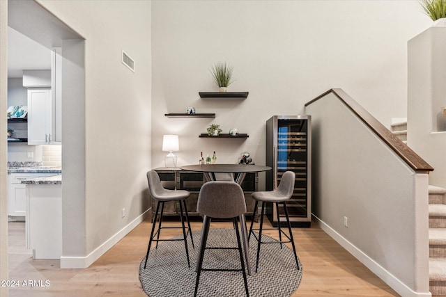 bar featuring white cabinets, decorative backsplash, wine cooler, and light hardwood / wood-style flooring