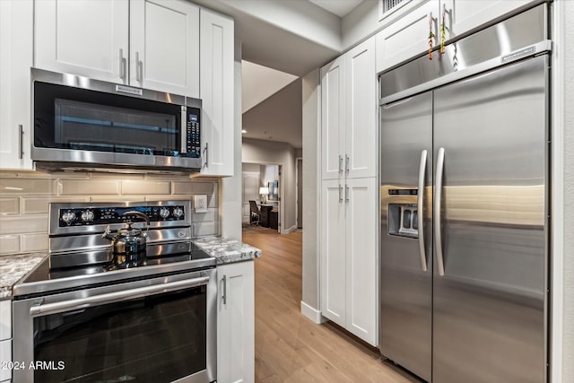 kitchen with light stone counters, white cabinets, stainless steel appliances, and light hardwood / wood-style floors