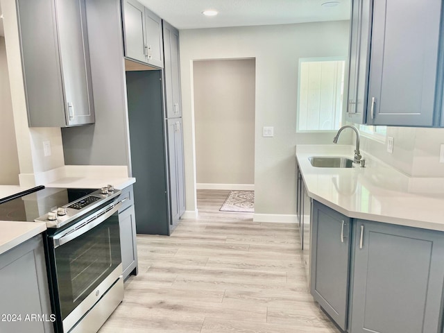 kitchen featuring a sink, stainless steel electric range oven, gray cabinets, and light wood finished floors