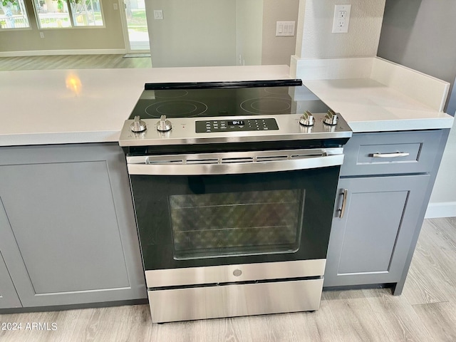 room details with stainless steel electric stove, light wood-style flooring, gray cabinetry, and light countertops
