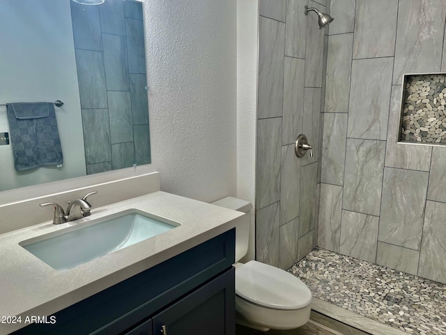 full bathroom with vanity, toilet, a textured wall, and a tile shower