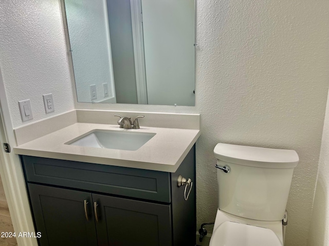 half bath featuring vanity, toilet, and a textured wall