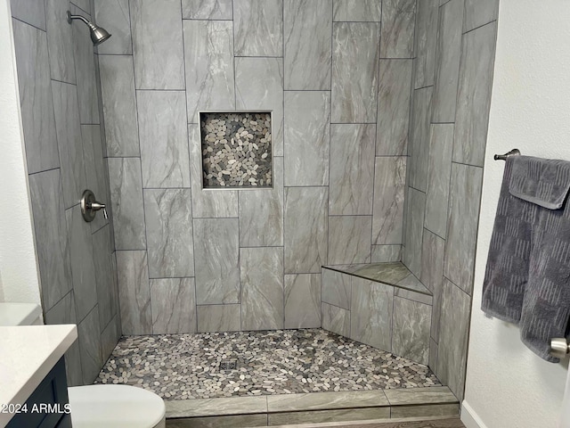 bathroom featuring a textured wall, toilet, vanity, and a tile shower
