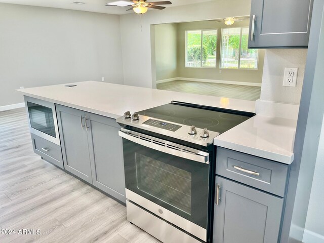 kitchen featuring a ceiling fan, gray cabinetry, stainless steel appliances, light countertops, and light wood-type flooring