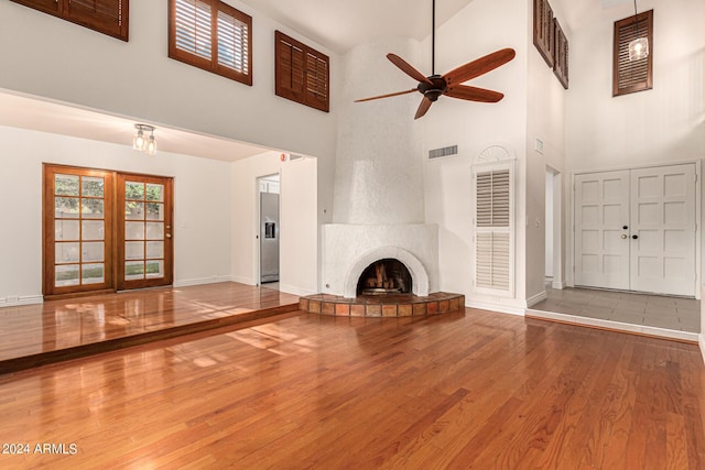 unfurnished living room featuring ceiling fan, a large fireplace, hardwood / wood-style floors, and a high ceiling