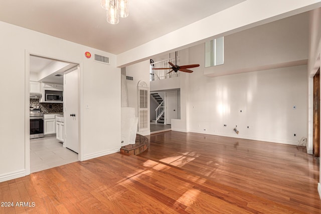 unfurnished living room with ceiling fan with notable chandelier, light hardwood / wood-style flooring, and a high ceiling