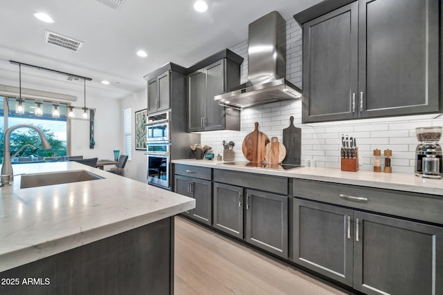 kitchen with wall chimney range hood, sink, hanging light fixtures, light wood-type flooring, and black electric cooktop