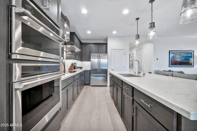 kitchen with decorative light fixtures, tasteful backsplash, a center island with sink, black appliances, and sink