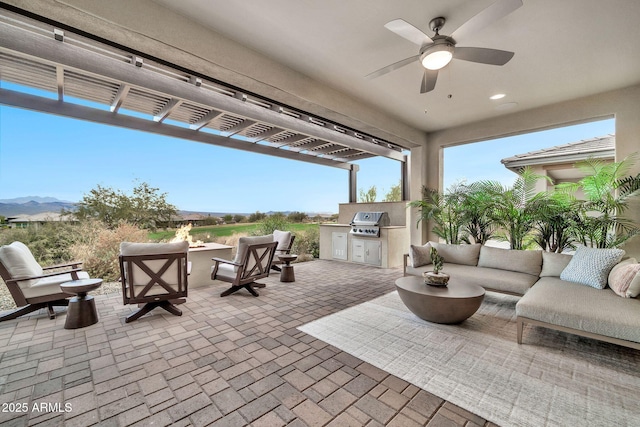 view of patio featuring a mountain view, ceiling fan, exterior kitchen, a grill, and an outdoor living space