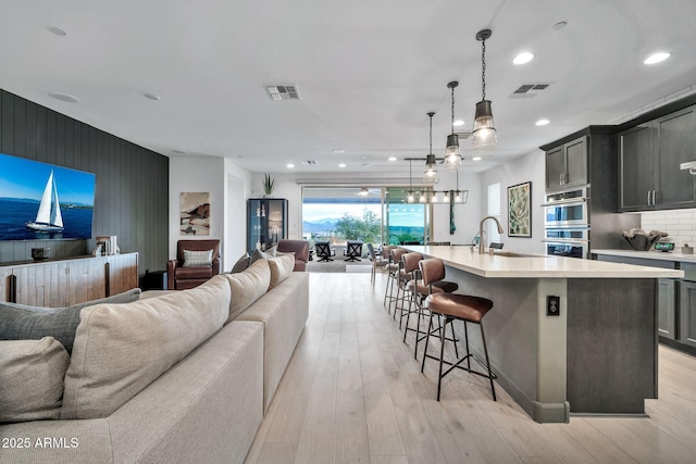 kitchen featuring an island with sink, light hardwood / wood-style floors, sink, hanging light fixtures, and decorative backsplash