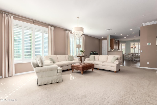 living area featuring light carpet, baseboards, visible vents, and a notable chandelier