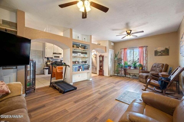 living room with light wood-type flooring, a ceiling fan, arched walkways, and built in shelves