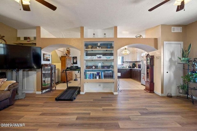 exercise room featuring arched walkways, visible vents, light wood finished floors, and ceiling fan