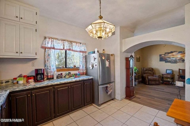 kitchen with an inviting chandelier, light tile patterned floors, arched walkways, freestanding refrigerator, and white cabinetry