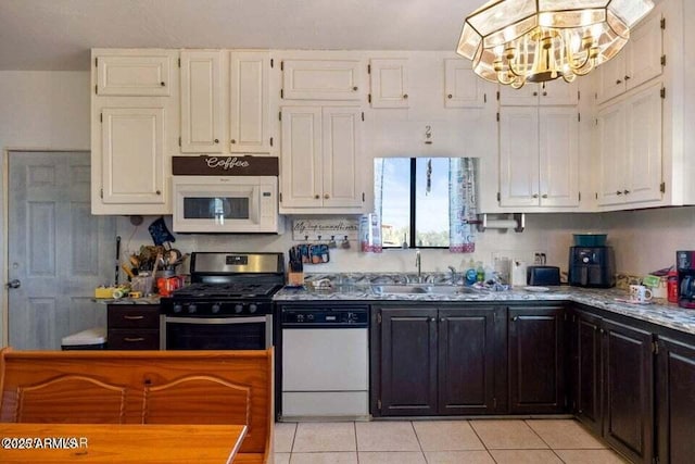 kitchen with a sink, white appliances, light tile patterned floors, an inviting chandelier, and white cabinetry