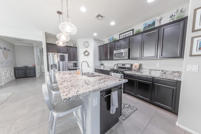 kitchen featuring visible vents, light stone counters, a breakfast bar, stainless steel appliances, and a sink