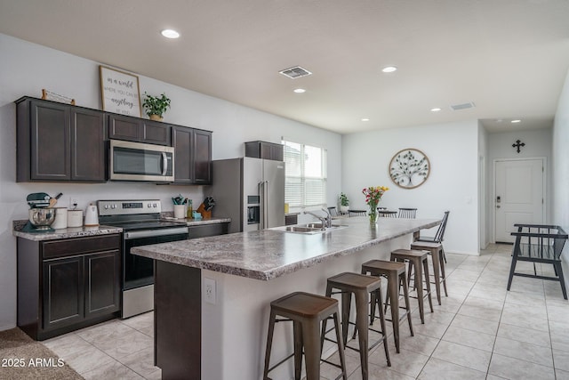 kitchen with sink, a kitchen breakfast bar, dark brown cabinetry, stainless steel appliances, and a center island with sink