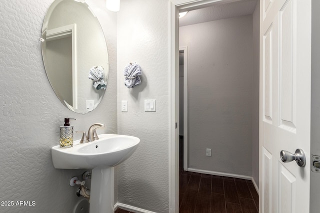 bathroom with wood tiled floor, a textured wall, and baseboards