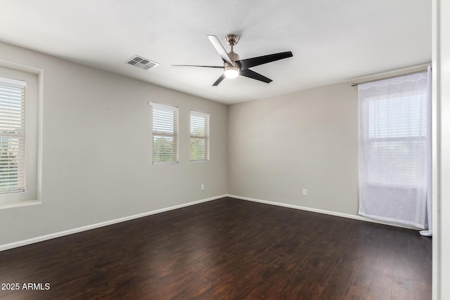 empty room featuring ceiling fan, visible vents, baseboards, and dark wood-style flooring