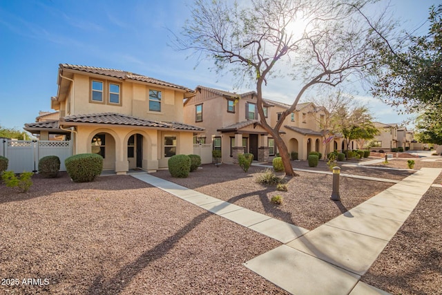 mediterranean / spanish-style home featuring covered porch, a tiled roof, fence, and stucco siding