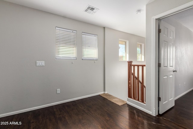 empty room with dark wood-style flooring, visible vents, and baseboards