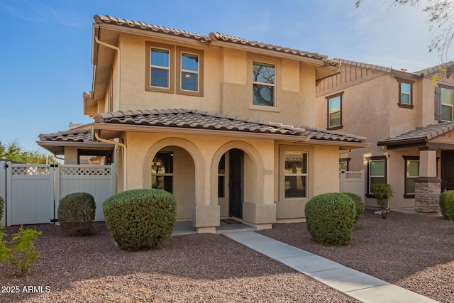 mediterranean / spanish home with a tile roof, fence, a gate, and stucco siding