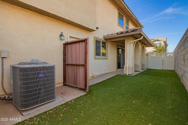 rear view of house with a yard, fence, central AC unit, and stucco siding