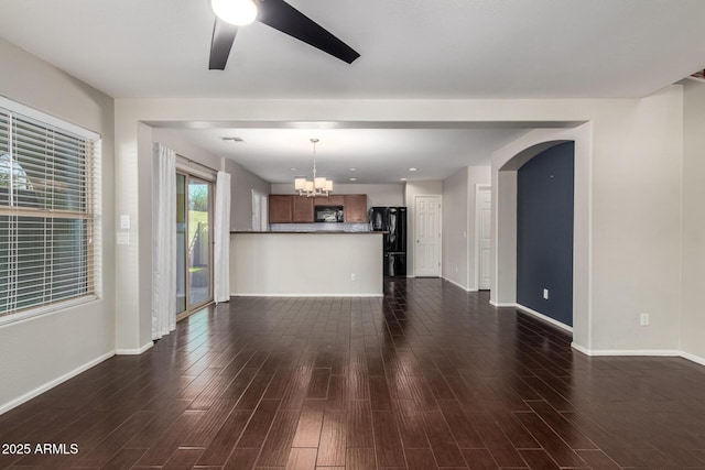 unfurnished living room featuring dark wood-style floors, baseboards, arched walkways, and ceiling fan with notable chandelier