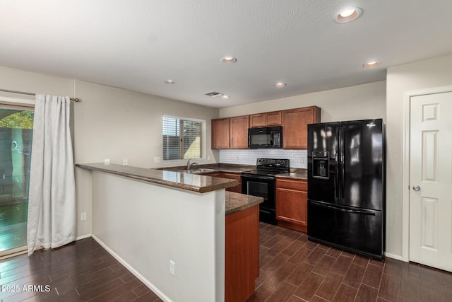 kitchen with a peninsula, wood finish floors, a sink, brown cabinets, and black appliances