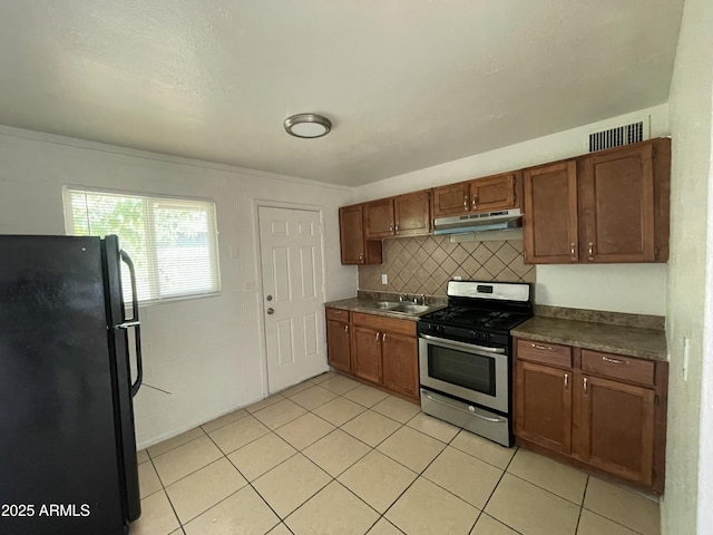 kitchen with tasteful backsplash, black fridge, ornamental molding, gas range, and sink