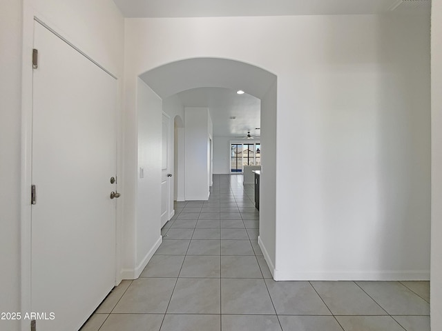 hall featuring light tile patterned floors, arched walkways, and baseboards