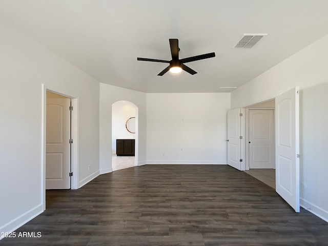 empty room with arched walkways, dark wood-style flooring, visible vents, and ceiling fan