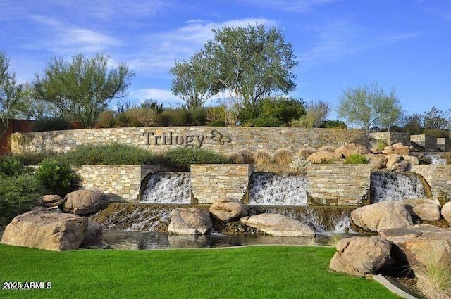 community sign featuring a small pond and a lawn