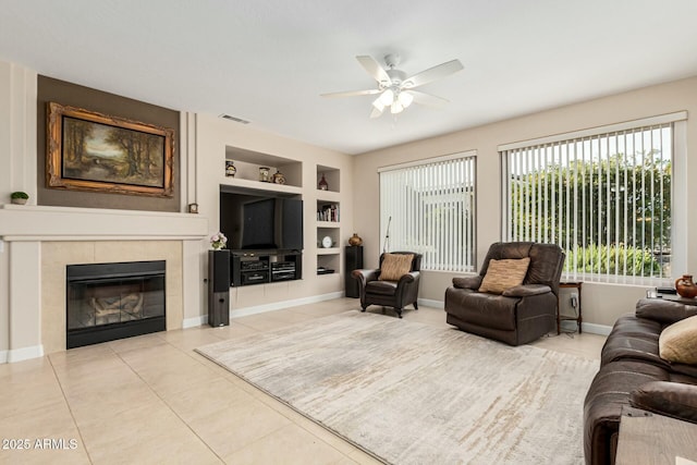 tiled living room with a fireplace, built in features, and ceiling fan