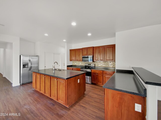 kitchen featuring appliances with stainless steel finishes, decorative backsplash, sink, a kitchen island with sink, and dark wood-type flooring