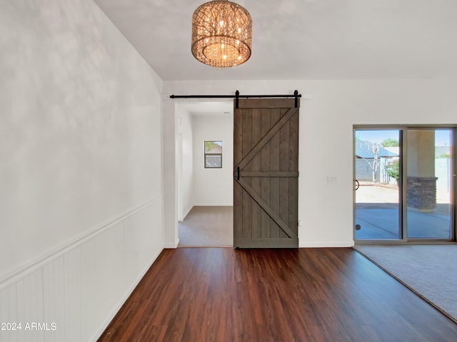 empty room with a notable chandelier, hardwood / wood-style flooring, and a barn door