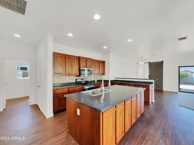 kitchen featuring backsplash, dark wood-type flooring, an island with sink, sink, and stainless steel appliances