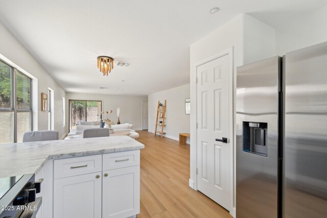 7500 E Deer Valley Rd Unit 132, Scottsdale, AZ 85255 - kitchen with stainless steel refrigerator with ice dispenser, white cabinets, light wood-type flooring, open floor plan, and light stone counters