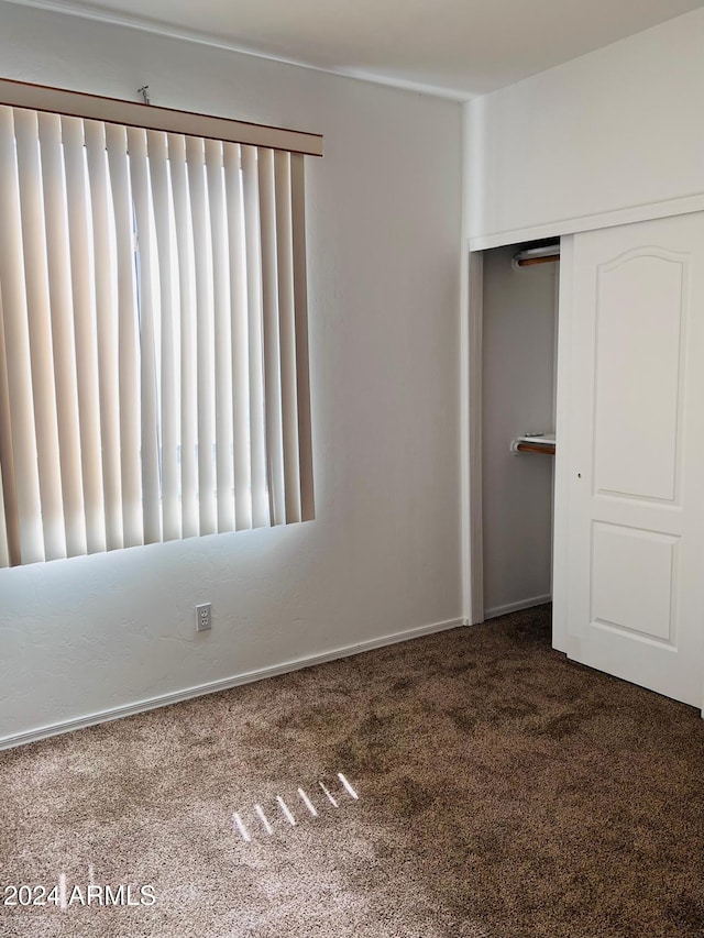 unfurnished bedroom with dark carpet and a closet