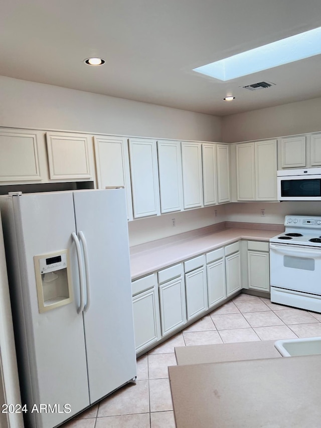 kitchen featuring a skylight, white cabinets, white appliances, and light tile patterned flooring