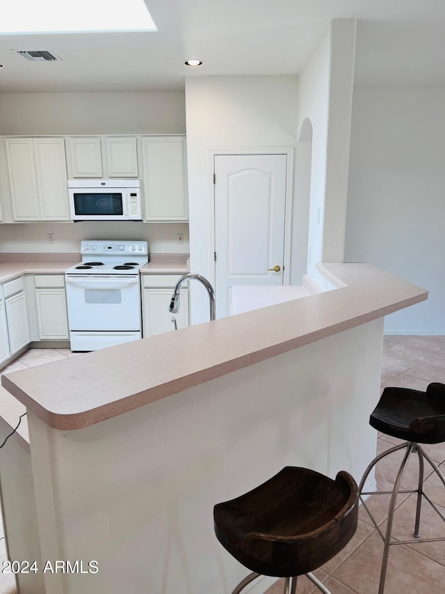 kitchen with white cabinets, a kitchen breakfast bar, light tile patterned flooring, sink, and white appliances