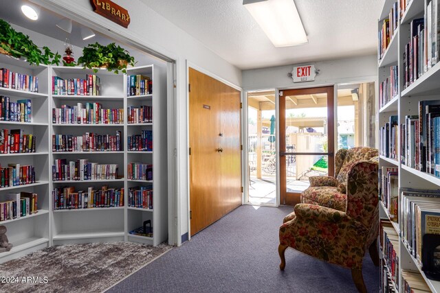 living area with carpet, a textured ceiling, and wall of books