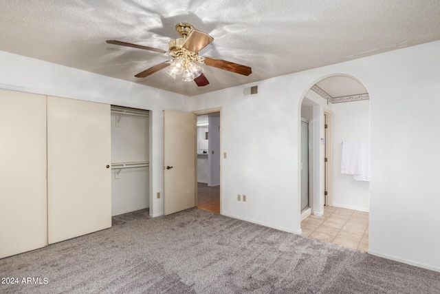 unfurnished bedroom with arched walkways, a textured ceiling, carpet, and visible vents